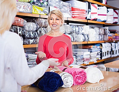 Aged female seller demonstrating coverlets to young buyer Stock Photo