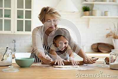 Aged grandma involve small grandkid in rolling dough with pin Stock Photo
