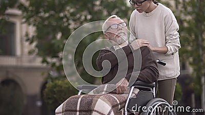 Aged sad disabled male in wheelchair covering young lady hand, family support Stock Photo