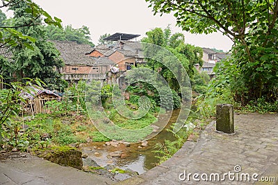 Aged tile-roofed brick houses on grassy brook shore after summer rain Stock Photo