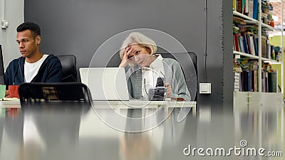 Aged woman, senior intern looking uncertain, confused at the screen while using laptop, sitting at desk, working in Stock Photo