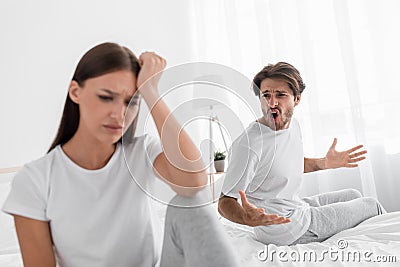 Aggressive evil millennial caucasian husband with stubble shouts and swears at offended sad depressed wife in bedroom Stock Photo