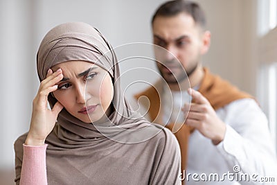 Aggressive Muslim Husband Shouting At Depressed Wife Standing At Home Stock Photo