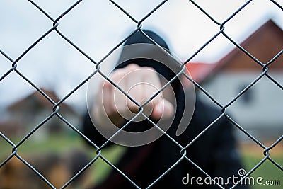 Aggressive teenage boy showing hes fist behind wired fence at the correctional institute, focus on the wired fence Stock Photo