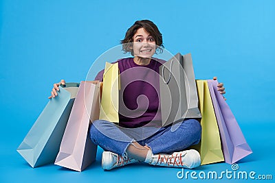 Agitated young pretty dark haired curly female with short haircut raising surprisedly eyebrows while looking at camera, sitting Stock Photo