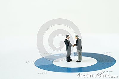 Agreement or deal for business success, miniature executive businessmen handshaking on printed performance pie chart or graph wit Stock Photo