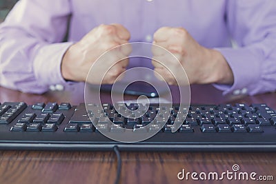 Agression in the Internet, man sitting behind keyboard with hands fists clenched Stock Photo