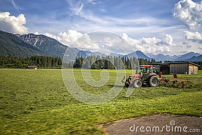 Agricultural machinery, a tractor collecting grass in a field against a blue sky. Stock Photo