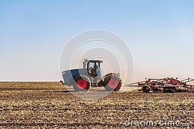 Agricultural tractor is working in the field under blue sky at daylight. Soil cultivation. Stock Photo