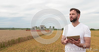 An agronomist stands with a tablet in a wheat field, a combine works in the background. A combine harvester harvests Stock Photo