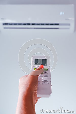 Air conditioning. A woman holds a remote control from an air conditioner in her hands. Wall mounted air conditioner unit in the Stock Photo