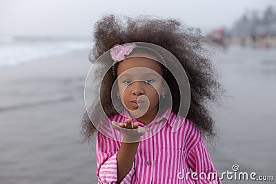 Air kiss. Playful girl with beautiful pink hair hoop in pink suit against background of sea. Stock Photo