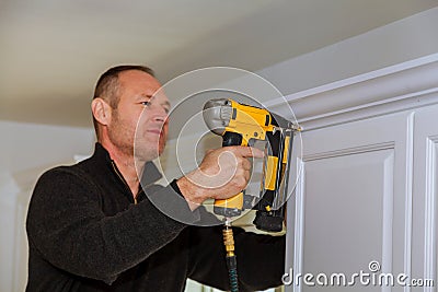 Air Nailer Tool, Carpenter using nail gun to crown moldings on kitchen cabinets Stock Photo