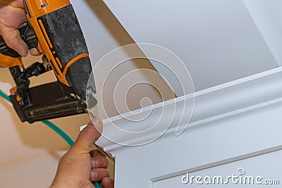 Air nailer tool carpenter using nail gun to crown moldings on kitchen cabinets with white cabinets Stock Photo
