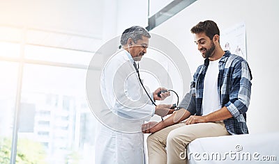 In with the air and out. a mature male doctor doing a check up on a young patient whos seated on a doctors bed. Stock Photo