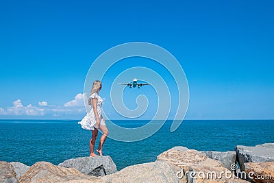 Airborne Encounters: Girl in White Dress on Stones, Plane Over the Blue Sea Stock Photo