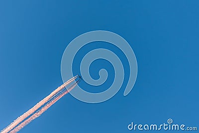 Airplane in a blue cloudless sky with colored colorful contrails without clouds during sunset and golden hour, Germany Stock Photo