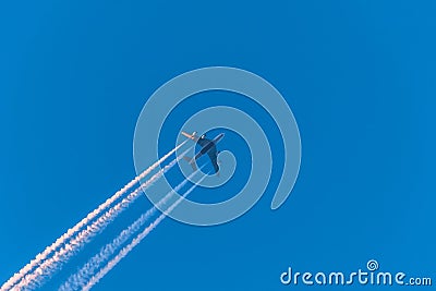 Airplane in a blue cloudless sky with colored colorful contrails without clouds during sunset and golden hour, Germany Editorial Stock Photo