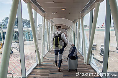Casual male passenger carrying the hand luggage bag, walking the airplane boarding corridor. Stock Photo