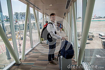 Airplane Boarding. Young male passenger carrying the hand luggage bag, walking the airplane boarding corridor. Stock Photo
