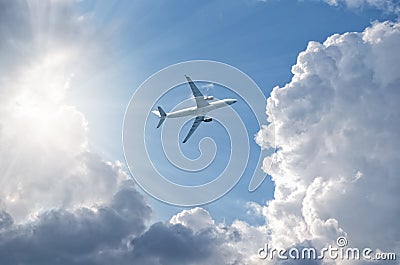 Airplane flying in blue sky, gaining height, sun shine through clouds, bottom view. Stock Photo