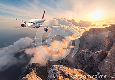 Landscape with white passenger airplane, mountains, sea and orange sky Stock Photo