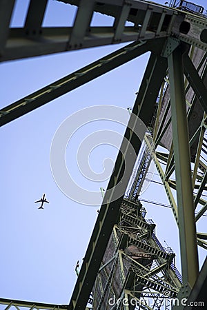 The plane flies over the triangular frames of the lifting bridge Stock Photo