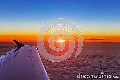 Airplane wing in flight above the clouds at the sunset background Stock Photo