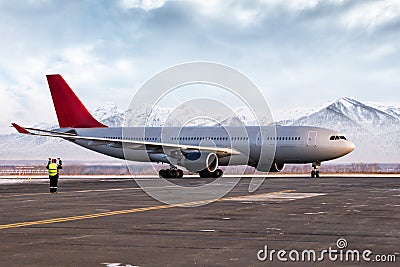 Airport marshaller meets passenger airliner on the background of high picturesque mountains Stock Photo