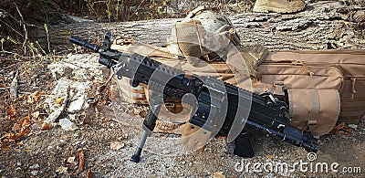 airsoft machine gun black next to a beige bag and helmet Stock Photo