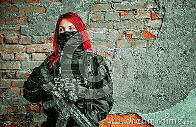 Airsoft red-hair woman in uniform with machine gun beside brick wall Stock Photo
