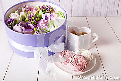 Airy and sweet handmade marshmallows on a white saucer next to a cup of tea and a box with a bouquet of marshmallow flowers Stock Photo