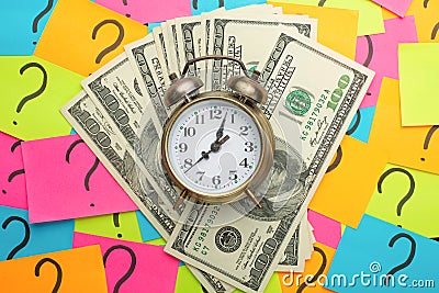 alarm clock on the background of question marks and US dollars, the concept of earning money, ideas for salary, and loss of time a Stock Photo