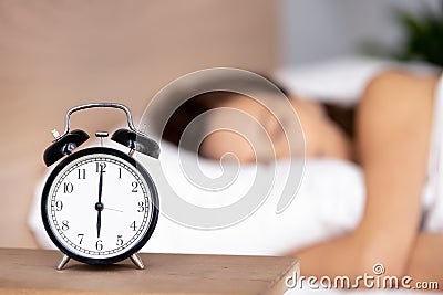 Alarm clock on bedside table with woman sleeping on background Stock Photo