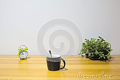 Alarm clock, coffee cup, and potted baby sun rose on home desk Stock Photo