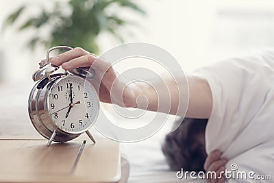 Alarm clock morning wake-up time on bedside table with man reaching to stop bell Stock Photo