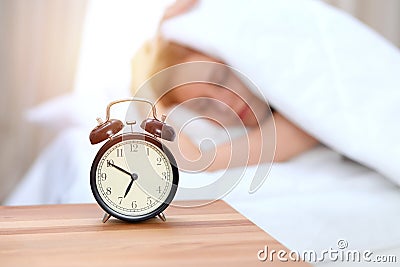 Alarm clock opposite of sleepy young woman. Early wake up, not getting enough sleep concept Stock Photo