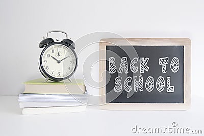 Alarm clock on a pile of books next to a blackboard with the text BACK TO SHOOL wrote on it. Empty copy space Stock Photo