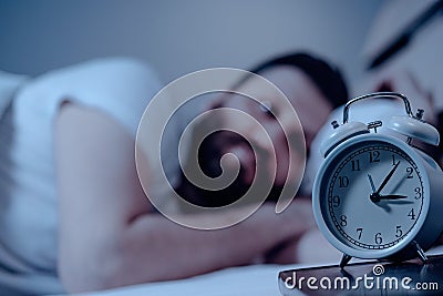 The alarm clock shows three in the morning, a man cannot fall asleep and watches the time. Insomnia, nightmare, bedroom, pajamas, Stock Photo