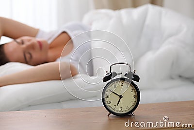 Alarm clock standing on bedside table has already rung early morning to wake up woman in bed sleeping in background Stock Photo