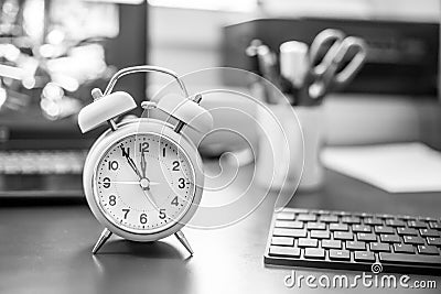 Alarm clock is standing on a grey desk, office stuff in the blurry background Stock Photo