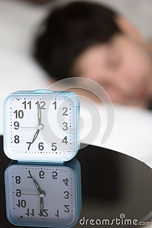 Alarm clock on table in front of sleeping man, vertical Stock Photo