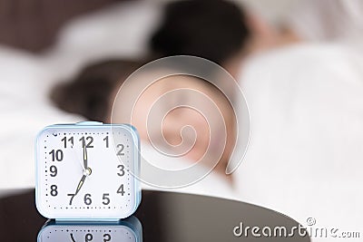 Alarm clock on table in front of sleeping young couple Stock Photo