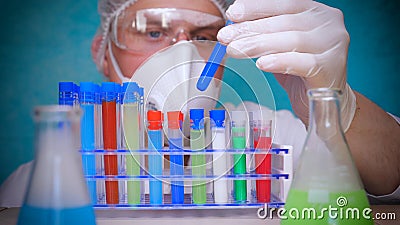 The alchemist checks the test tubes with a test of different compositions, in a white coat, a respirator, goggles, rubber white gl Stock Photo