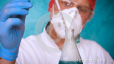 The alchemist checks the test tubes with a test of different compositions, in a white coat, a respirator, goggles, rubber white gl Stock Photo