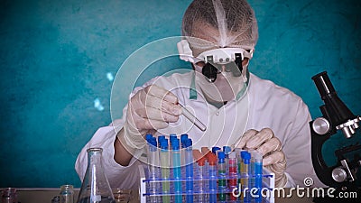 The alchemist checks the test tubes with a test of different compositions, in a white coat, a respirator, goggles, rubber white gl Stock Photo