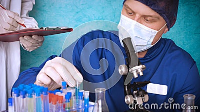 The alchemist checks the test tubes with a test of different compositions, in a white coat, a respirator, goggles, rubber white gl Stock Photo