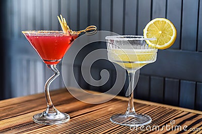 Alcohol cocktails Cosmopolitan and Margarita on wooden table against dark wall with copy space Stock Photo