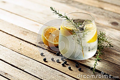 Alcohol drink gin tonic cocktail with lemon, juniper branch, and ice on rustic wooden table Stock Photo