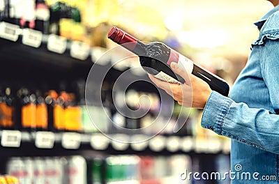 Alcohol shelf in liquor store or supermarket. Woman buying a bottle of red wine and looking at alcoholic drinks in shop. Stock Photo